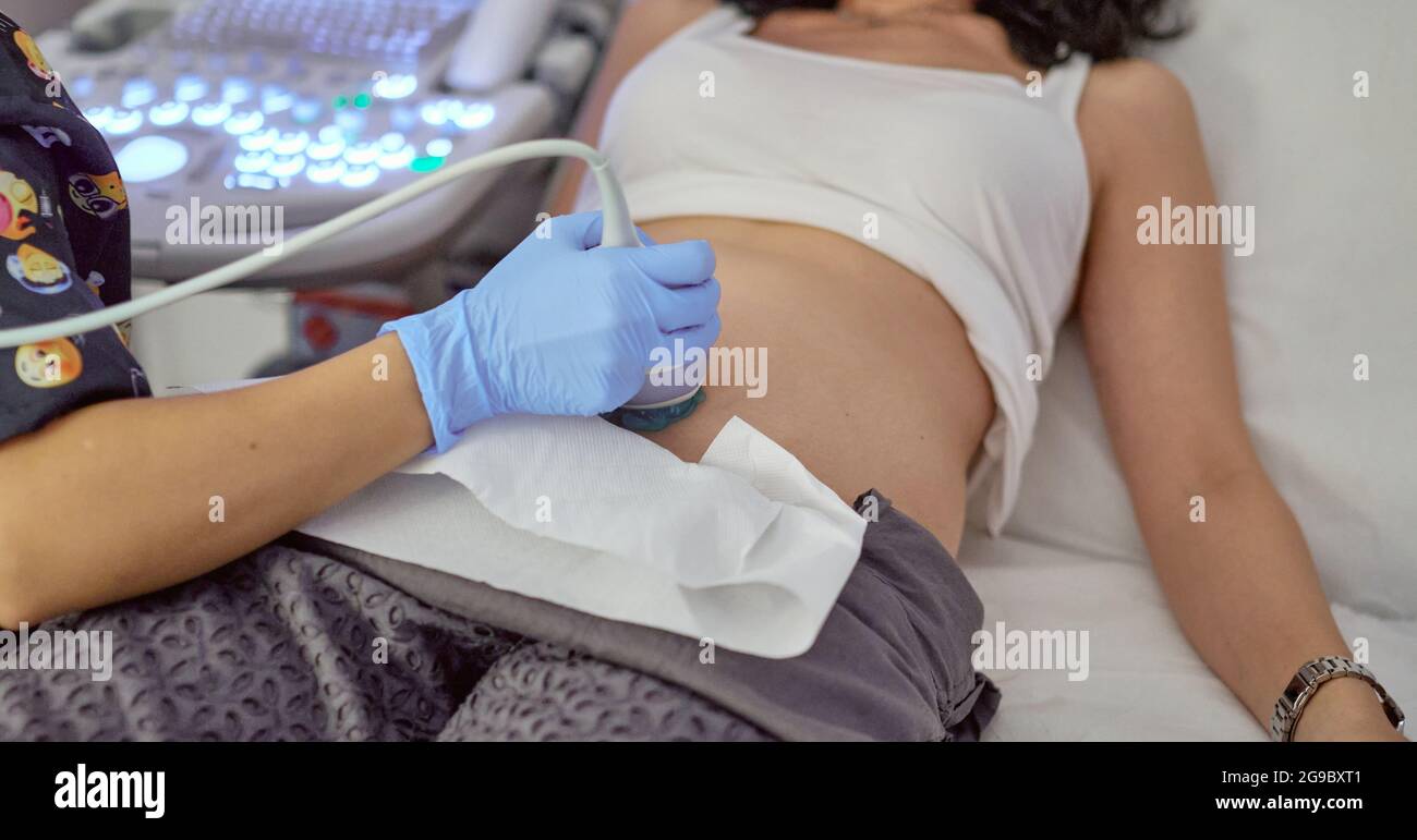 mano di un medico con un ecografo sul ventre di una donna incinta che fa un ecografo di controllo in una clinica Foto Stock