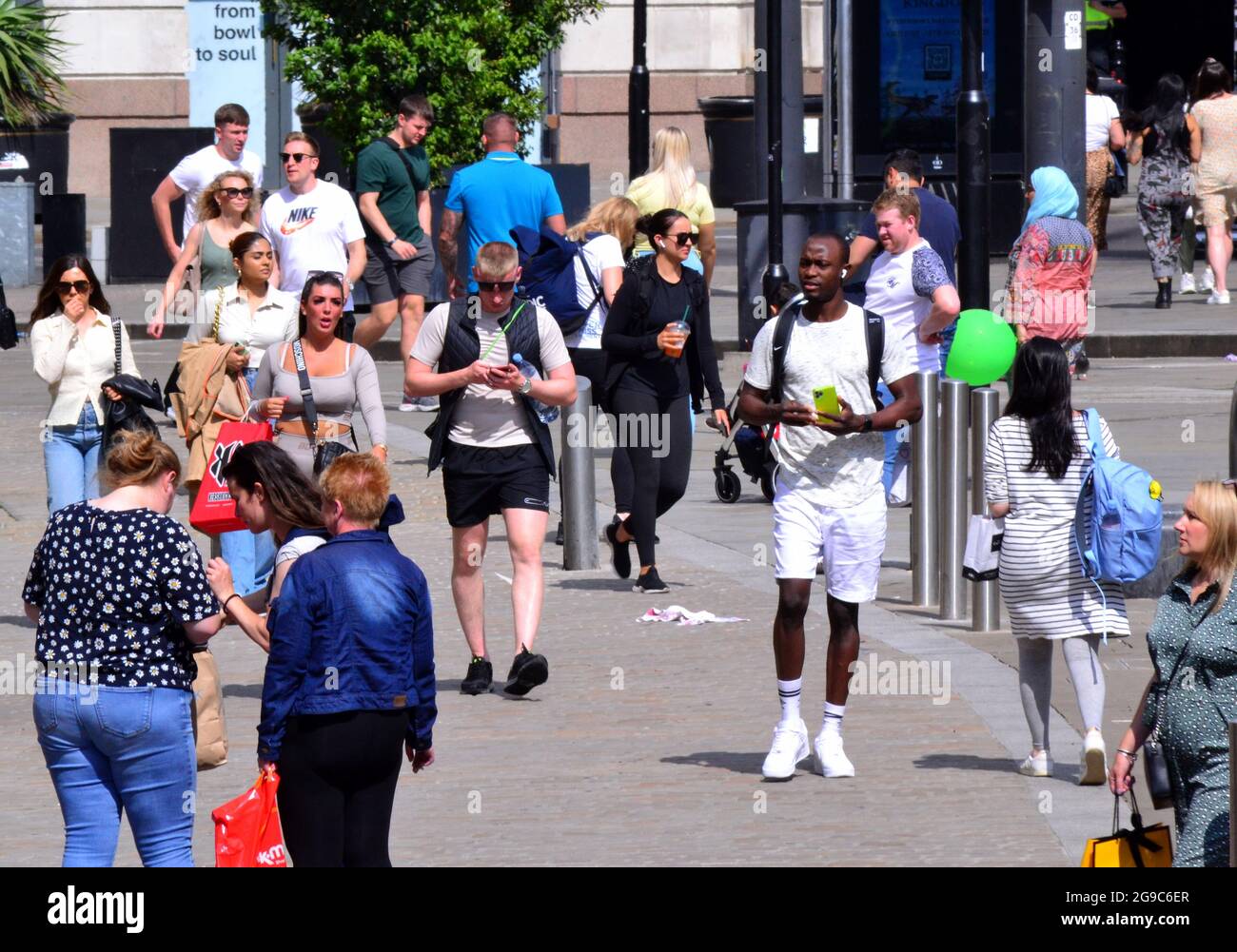 La gente gode del sole estivo che cammina all'aperto nel centro di Manchester, Inghilterra, Regno Unito. Foto Stock