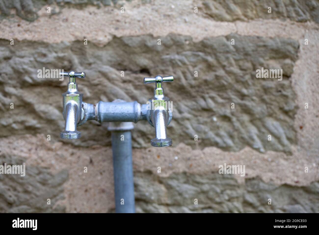 Due rubinetti in acciaio per esterni davanti ad un vecchio muro di arenaria Foto Stock