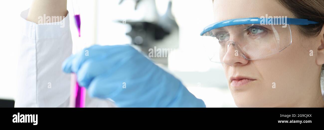 Donna chimico in occhiali protettivi gocciolando liquido rosa nel test tubo Foto Stock