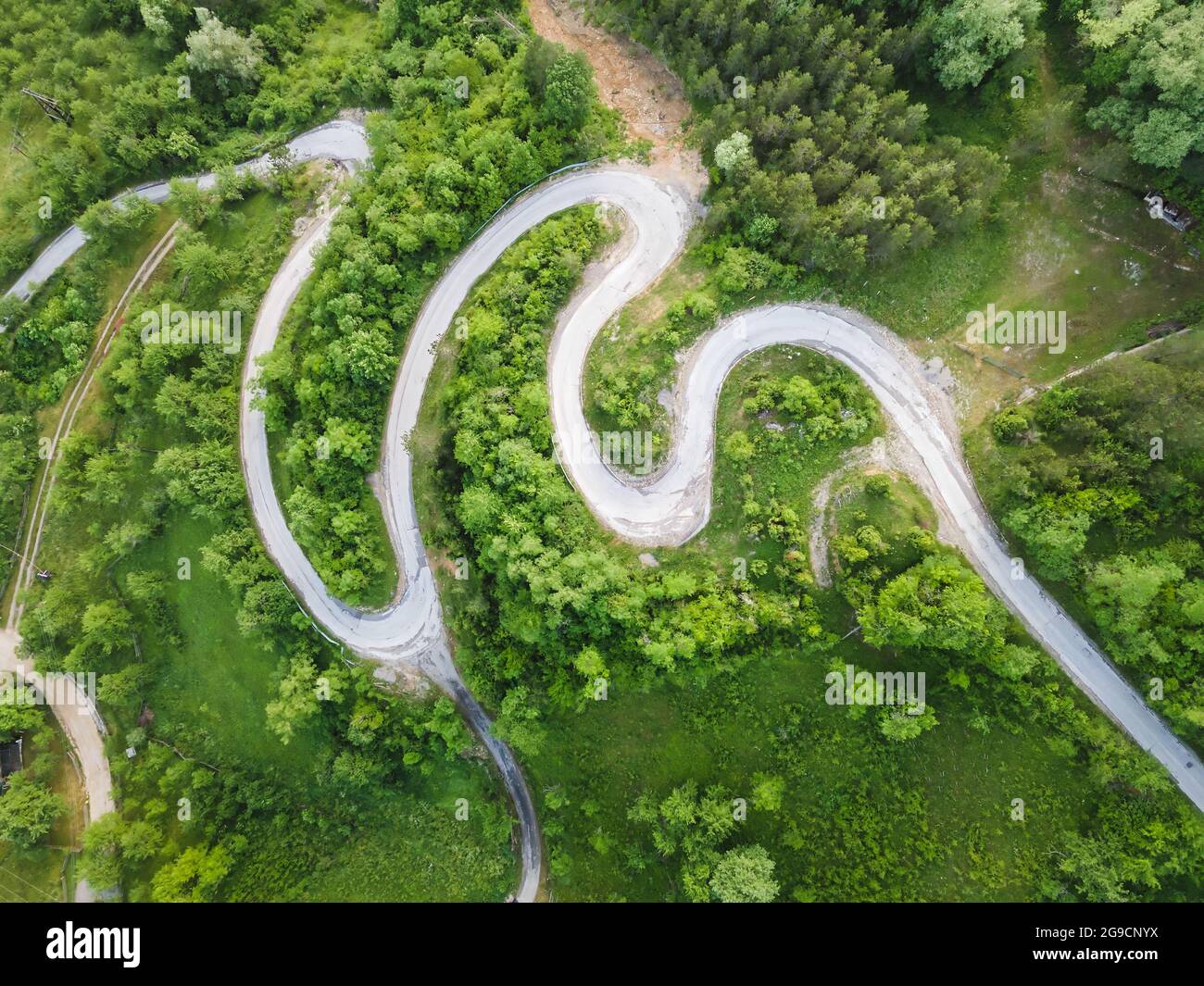 Vista sul drone della bellissima strada a serpentina che conduce attraverso il paesaggio montano in estate. Fotografia aerea di una foto di strada con un drone. Strada danneggiata Foto Stock