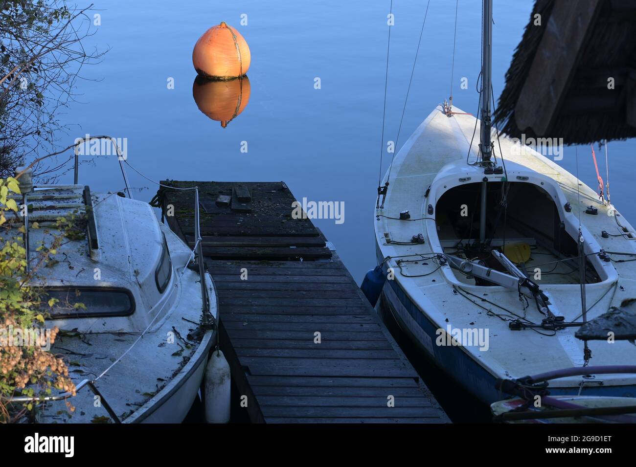 Due barche sporche in un molo e una boa arancione nelle acque blu e calme di un lago stanno aspettando la fine del covid-19 lockdown, copy space, selezionato fuoco Foto Stock