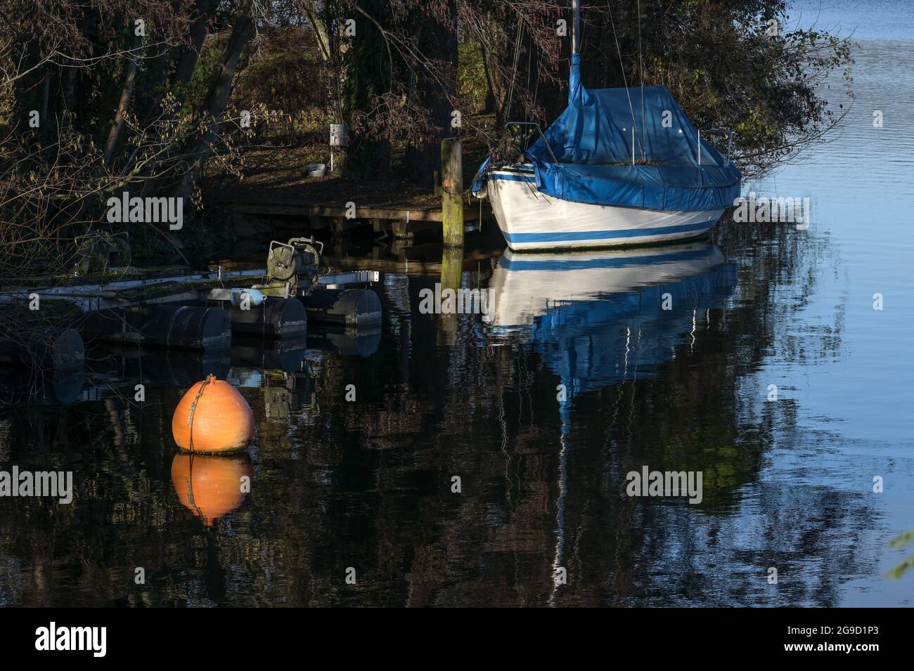 Barca a vela coperta con telone blu e una boa arancione nel lago sulla riva, attività di svago concetto, spazio copia, fuoco selezionato, profondità stretta Foto Stock
