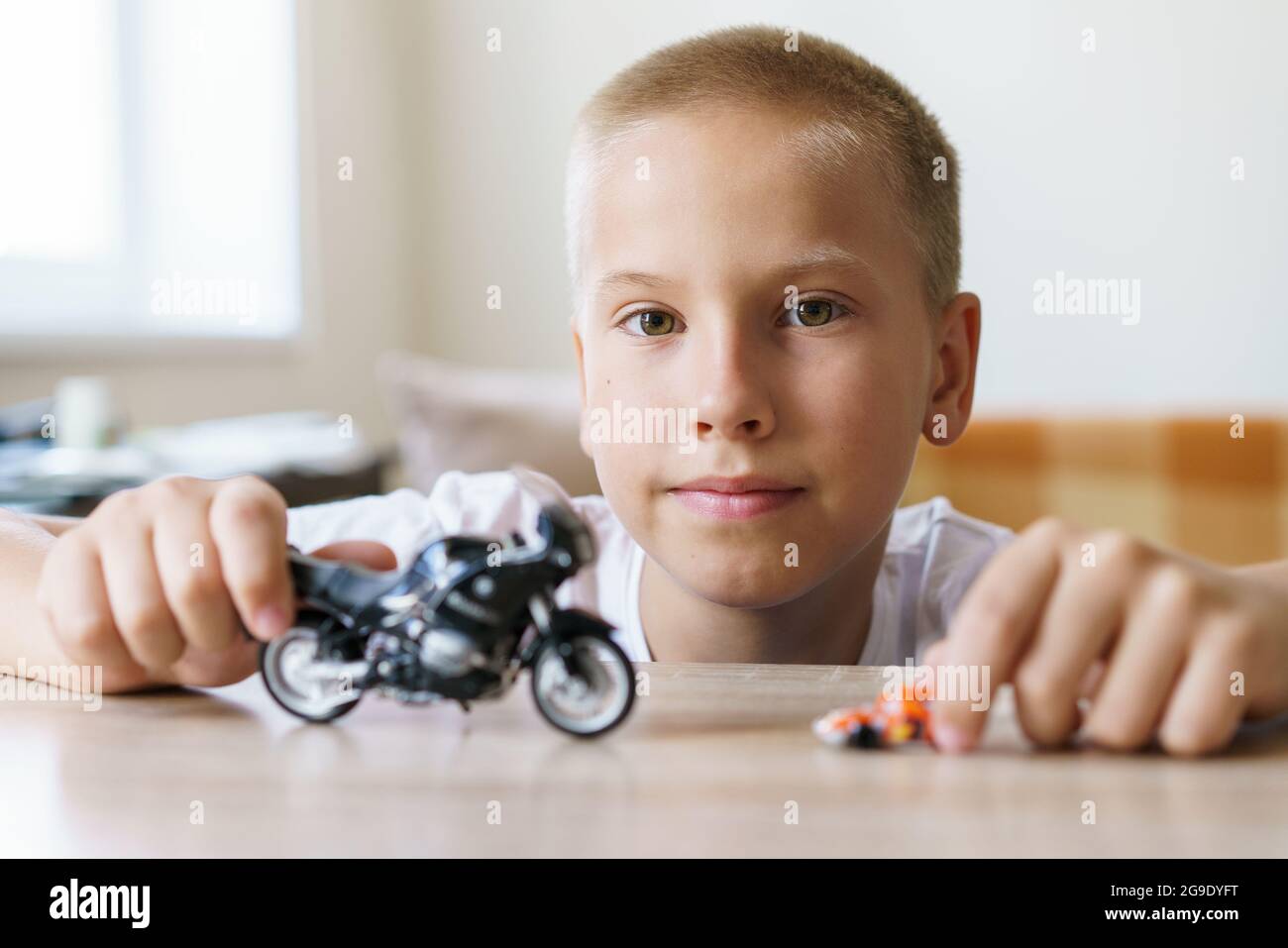 Carino ragazzo di età scolastica di aspetto europeo si siede sulla sedia a  tavola e gioca con una moto giocattolo. Concetto di sviluppo del bambino a  casa Foto stock - Alamy
