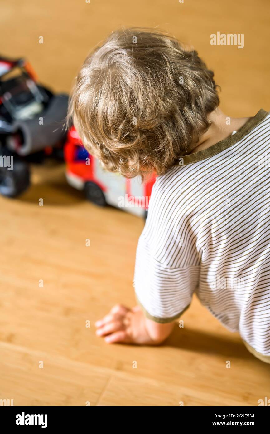 Un ragazzo dai capelli ricci gioca con entusiasmo con un'auto giocattolo e piccoli uomini in modo infantile immaginando una situazione di vita reale con il participant Foto Stock