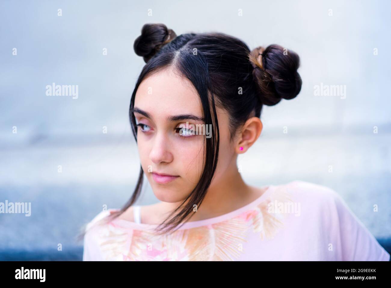 Bruna femminile elegante e raffinata per adolescenti con ciambelle di capelli che guardano via da sogno contro sfondo sfocato Foto Stock