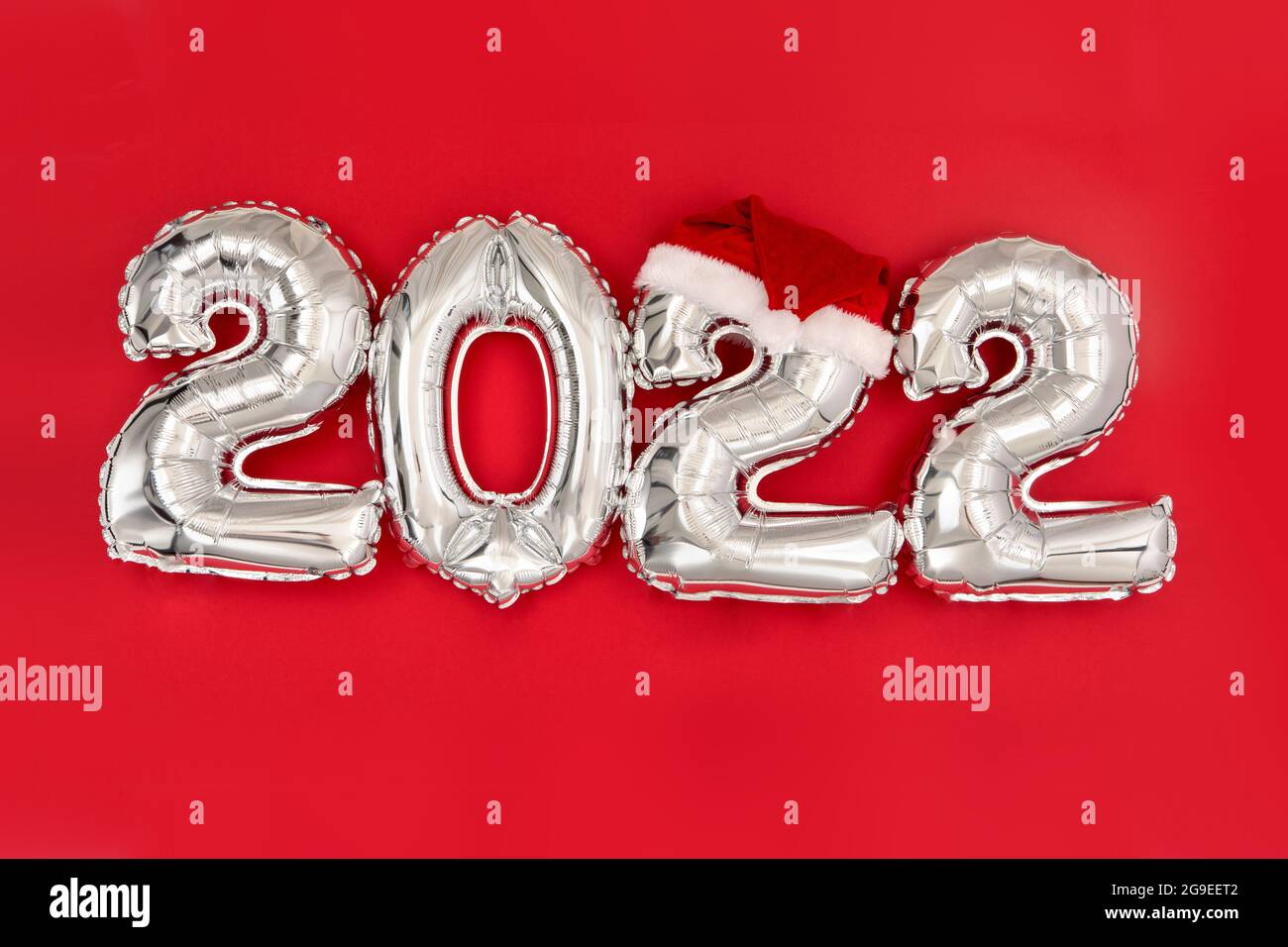 2022 palloncini gonfiabili su sfondo rosso con cappello santa. Felice celebrazione del nuovo anno 2022. Palloncini in lamina d'argento numero 2022. Cartoline e poster. Foto Stock
