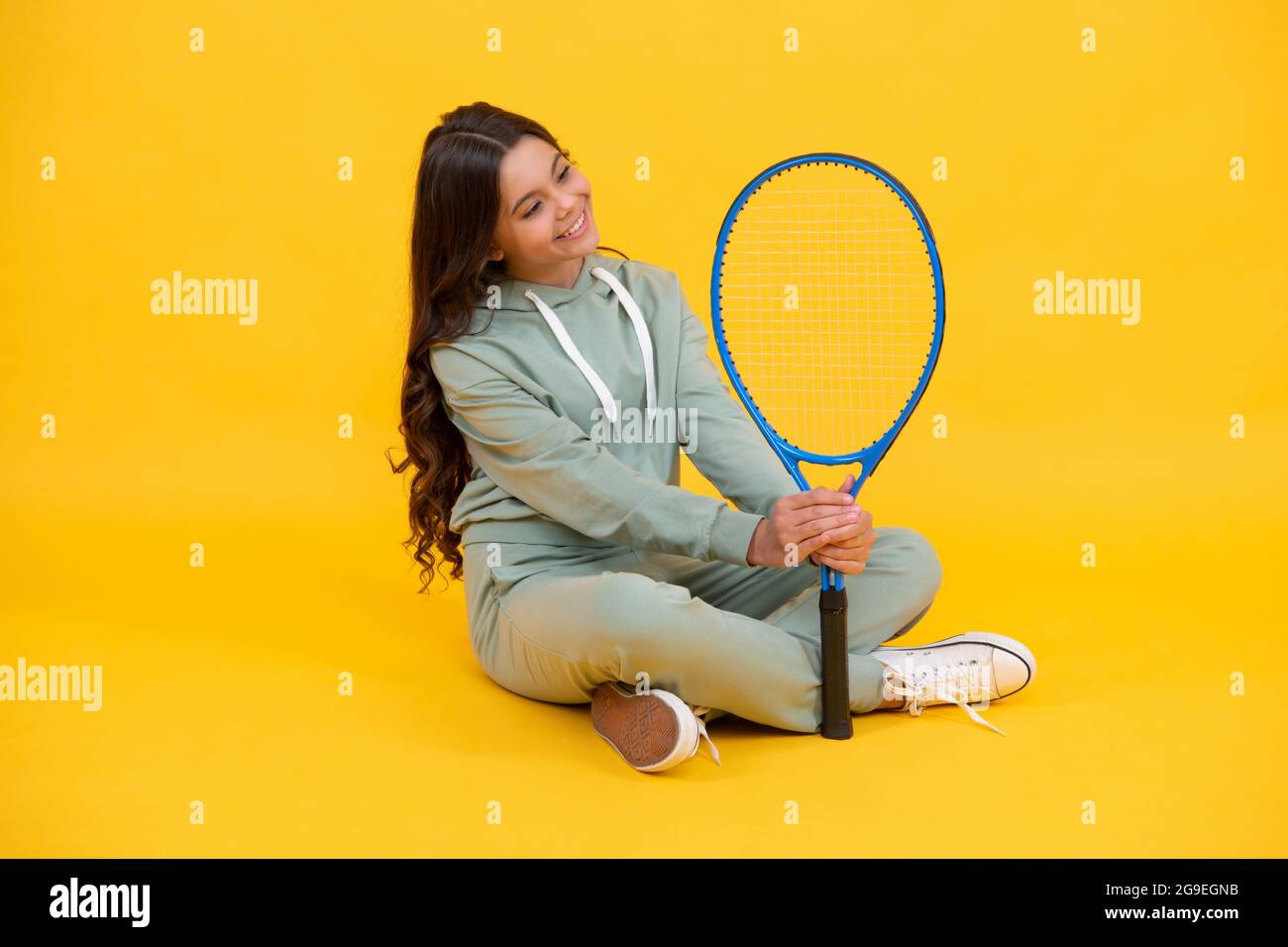 allegra ragazza teen in sportswear tenere racchetta tennis su sfondo giallo, sport Foto Stock