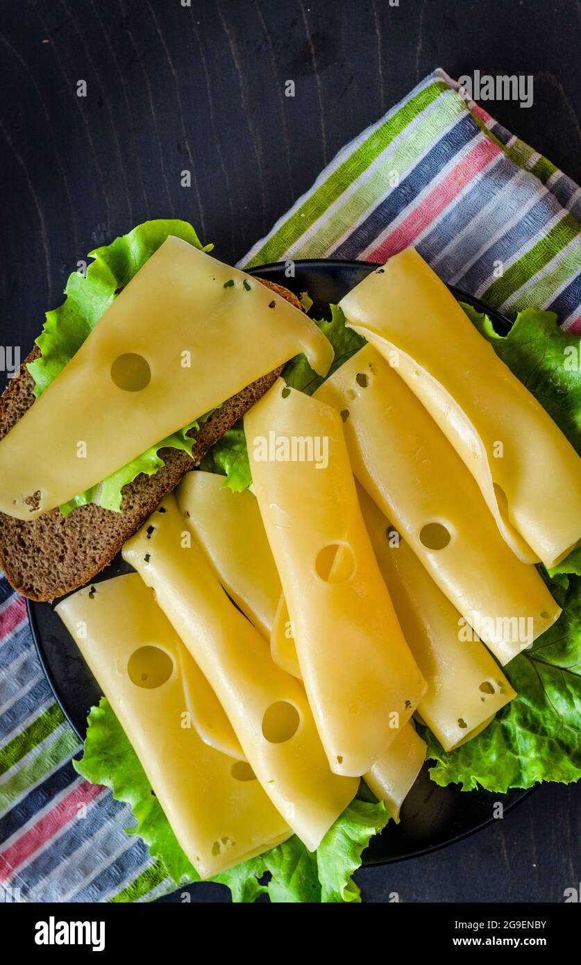 formaggio duro con grandi buchi tagliati su un piatto con foglie di lattuga Foto Stock