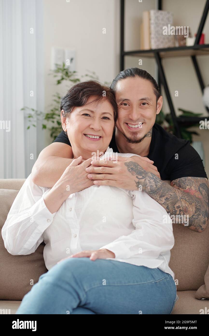 Ritratto della felice famiglia asiatica di due sorridenti con la macchina fotografica mentre si riposa sul divano nella stanza a casa Foto Stock