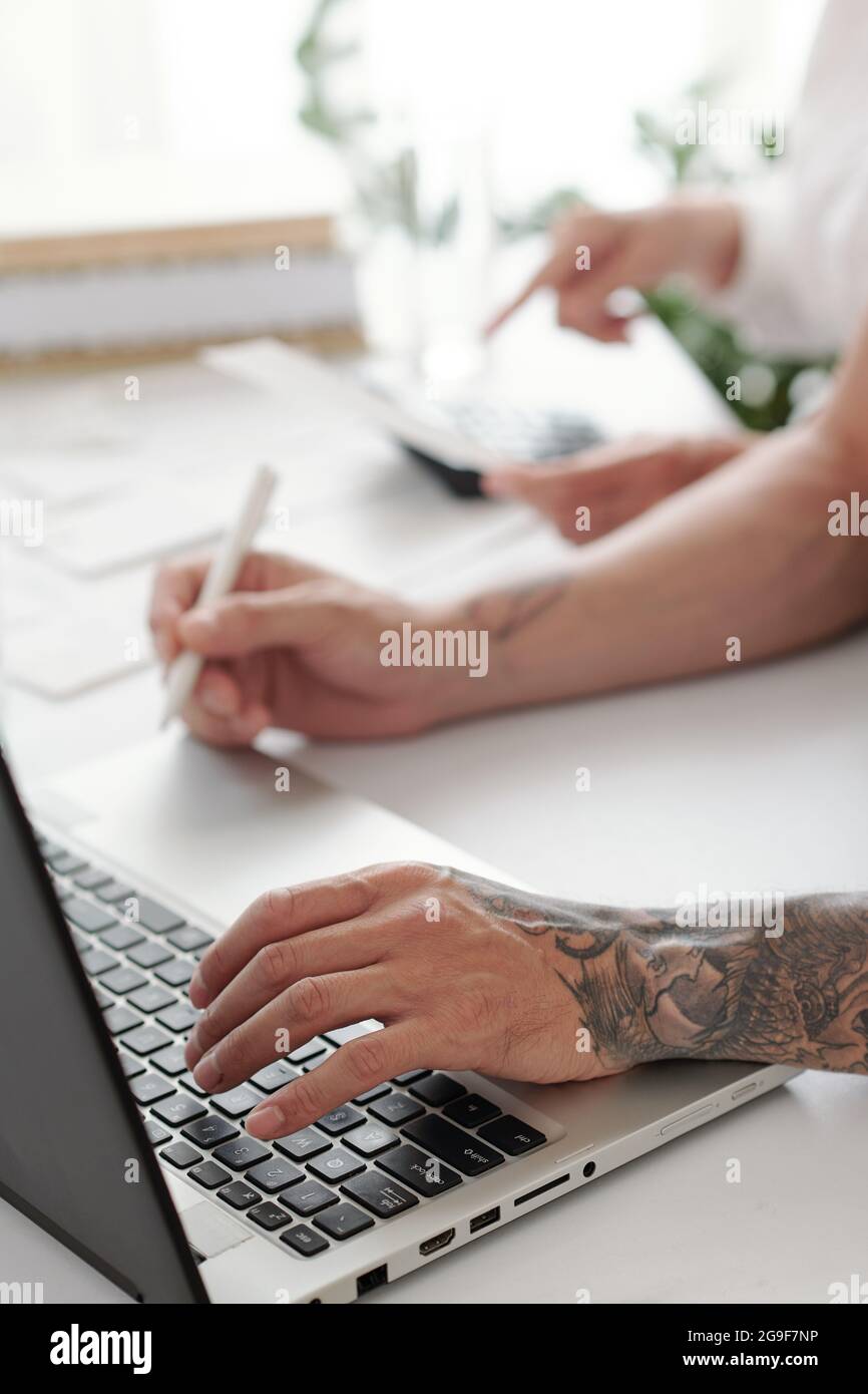 Primo piano di un uomo seduto al tavolo e che lavora su un computer portatile, scrive i documenti online in ufficio Foto Stock
