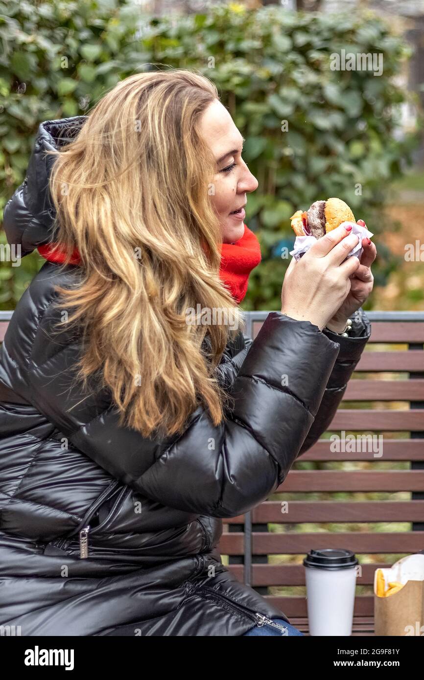 Giovane donna affamata mangia Burger e si prende pausa pranzo all'aperto nel Park.fast food. Concetto di cibo da asporto. Foto Stock