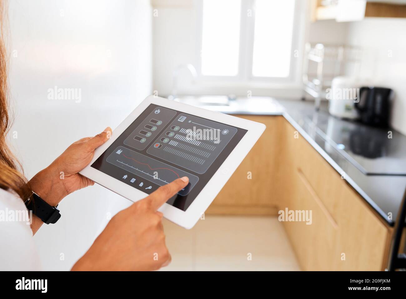 Mani di donna che usano l'applicazione sul computer tablet quando si imposta la temperatura e la luce in cucina Foto Stock
