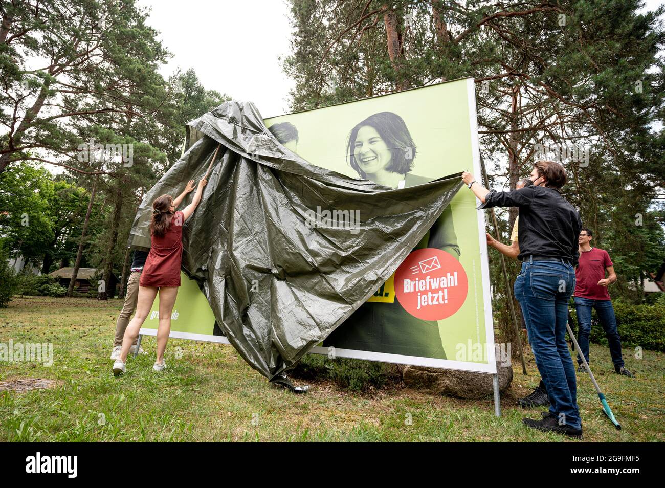 Michendorf, Germania. 26 luglio 2021. I membri del partito coprono il grande poster con l'iscrizione 'il nostro paese può fare molto se lo lasciate', parte della campagna del Partito Verde 'pronti, perché siete', prima della presentazione. Con questo, i Verdi hanno dato il via alla campagna a livello nazionale per le elezioni federali del 2021. La Presidente del Partito Verde sta candidando direttamente nel distretto elettorale 61 Potsdam - Potsdam-Mittelmark II - Teltow-Fläming II contro, tra gli altri, il candidato del DOCUP per il cancelliere O. Scholz. Credit: Fabian Sommer/dpa/Alamy Live News Foto Stock