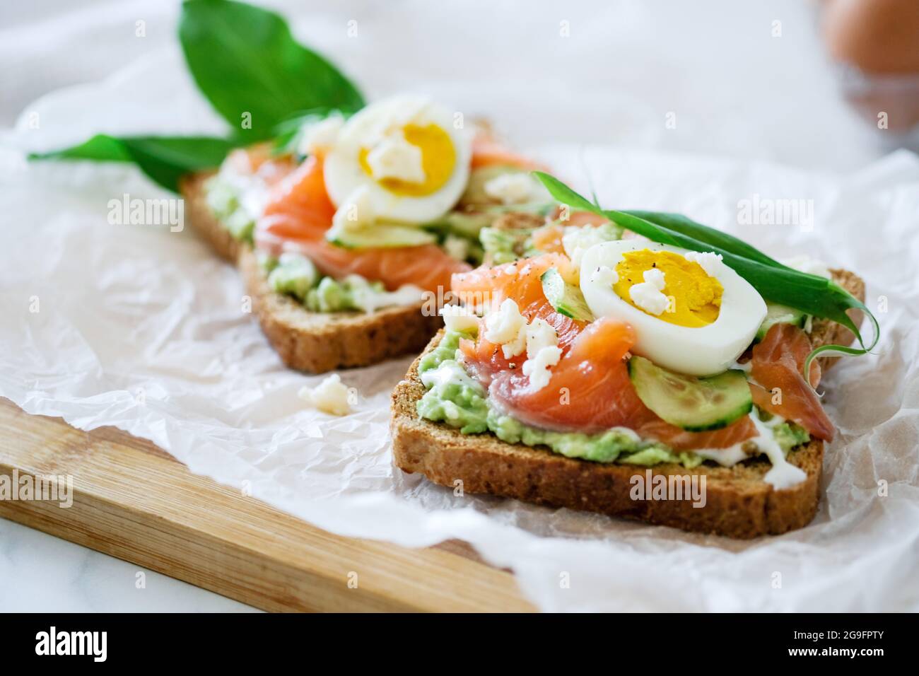 Sandwich aperto tradizionale danese Smorrebrod salmone, cetriolo, uova sode, formaggio morbido. Panino fatto in casa con pane di segale su sfondo bianco, vista dall'alto. Foto Stock