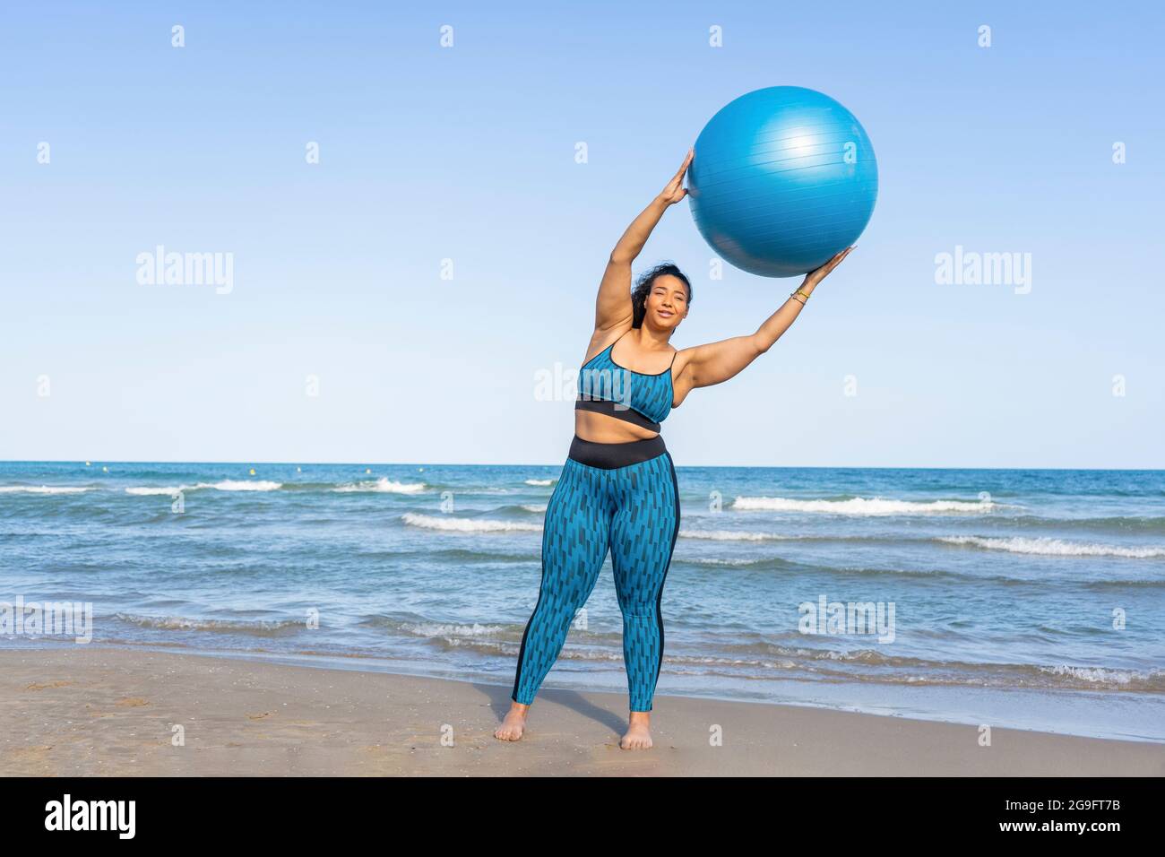 Donna che tiene una palla di fitness che fa yoga o pilates esercizi sulla spiaggia Foto Stock