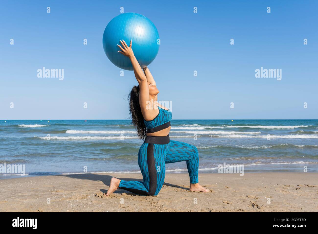 Donna che gioca con una palla fitness che fa esercizi sportivi sulla spiaggia Foto Stock