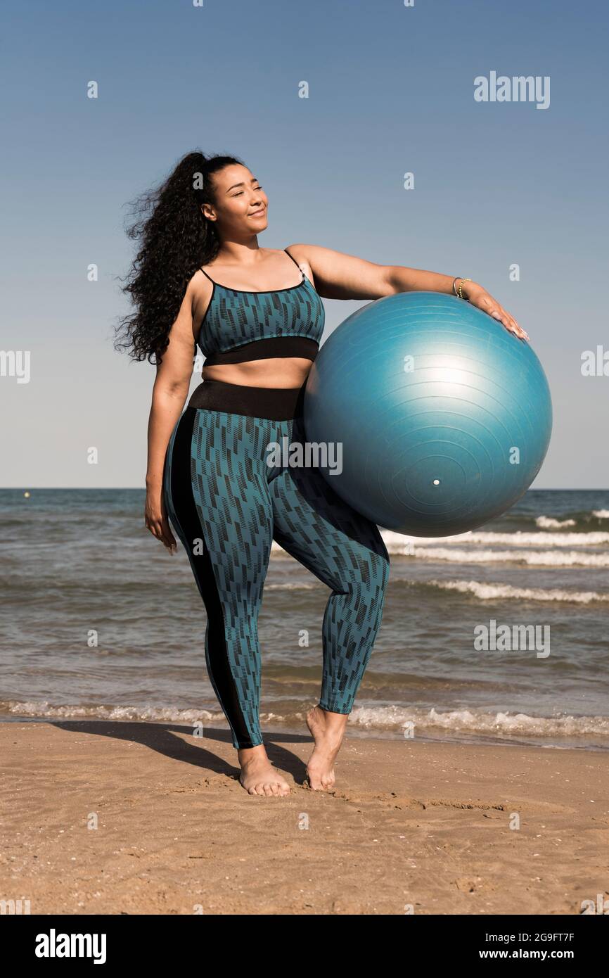 Donna che tiene una palla di fitness che fa yoga o pilates esercizi sulla spiaggia Foto Stock