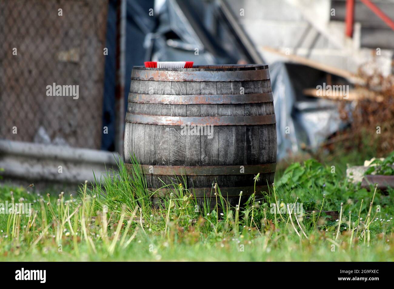 Retro vintage vecchia botte di legno grande vino con cerchi in metallo arrugginito e tavole di legno dilapidate a sinistra nel cortile suburbano casa di famiglia con rosso Foto Stock