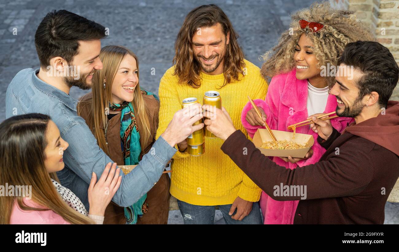 Gruppo multirazziale di giovani felici che si divertono per strada celebrando l'amicizia tostando con bevande in scatola. I Millennial che si riuniscono bevendo essere Foto Stock