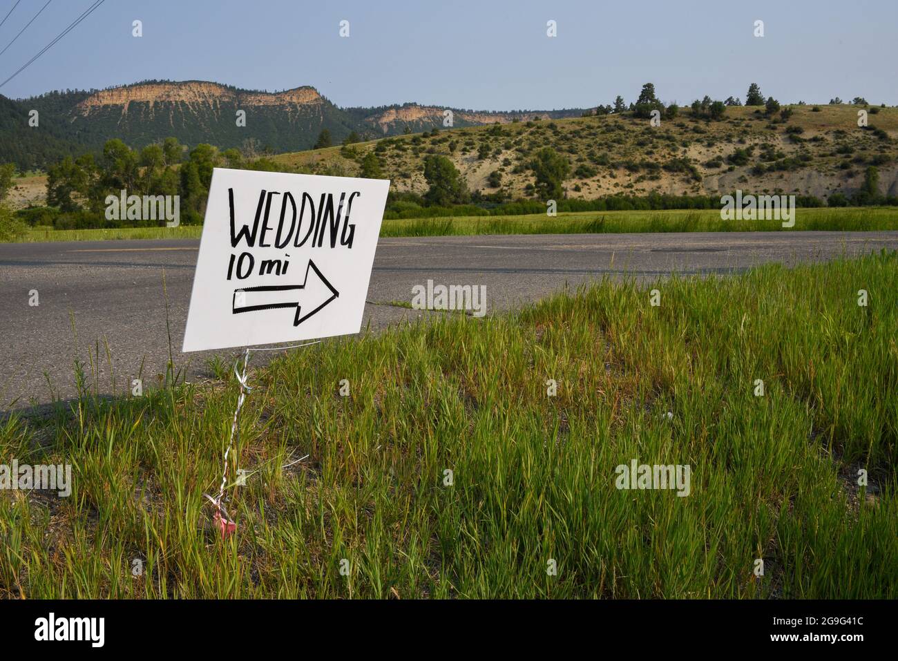 Un cartello bianco fatto a mano con scritta nera posto lungo un tratto remoto di autostrada in Colorado segna la strada per un matrimonio. Foto Stock