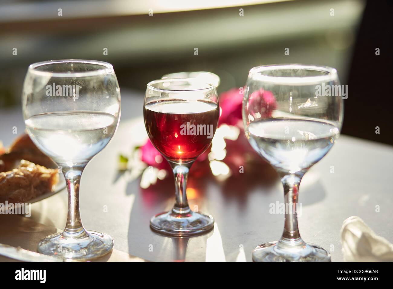 Bicchiere di vino rosso e bicchieri d'acqua sul tavolo. Decorazioni di fiori rosa bouganville. Spazio di copia. Foto Stock