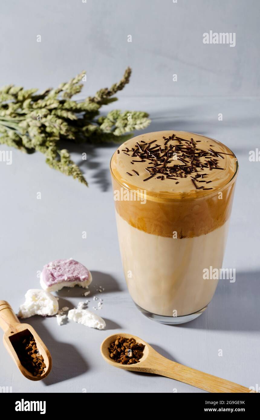 Caffè Dalgon in alto highball con gocce di cioccolato su sfondo grigio, cucchiai di legno con briciole di caffè Foto Stock