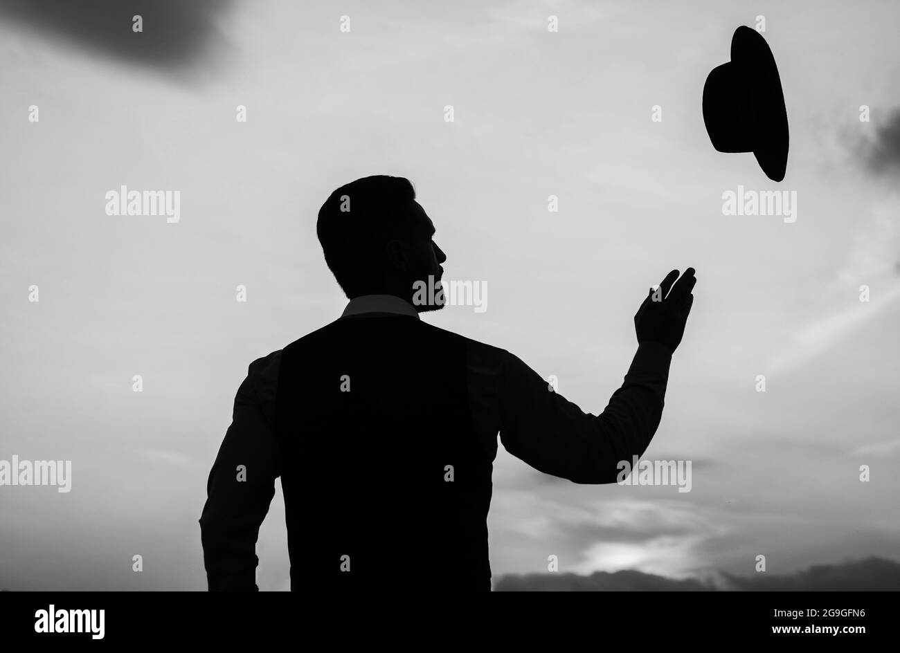 silhouette di uomo che getta il suo cappello sul cielo di alba, spensierato Foto Stock