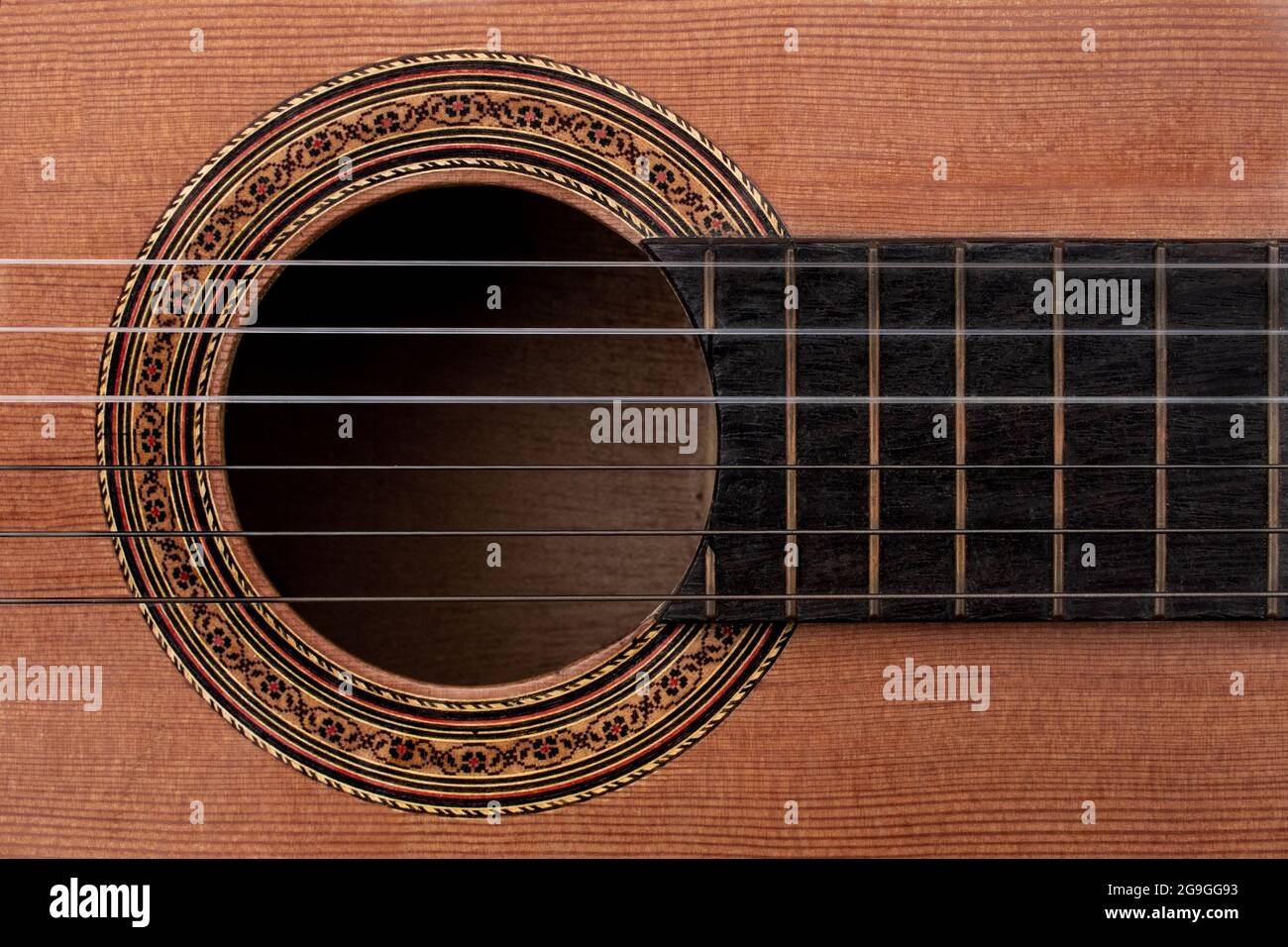 Primo piano di una vecchia chitarra acustica che mostra i dettagli della decalcomania di rosette decorative intorno al soundhole, alle corde e a parte della tastiera in ebano. Vista dall'alto verso il basso Foto Stock