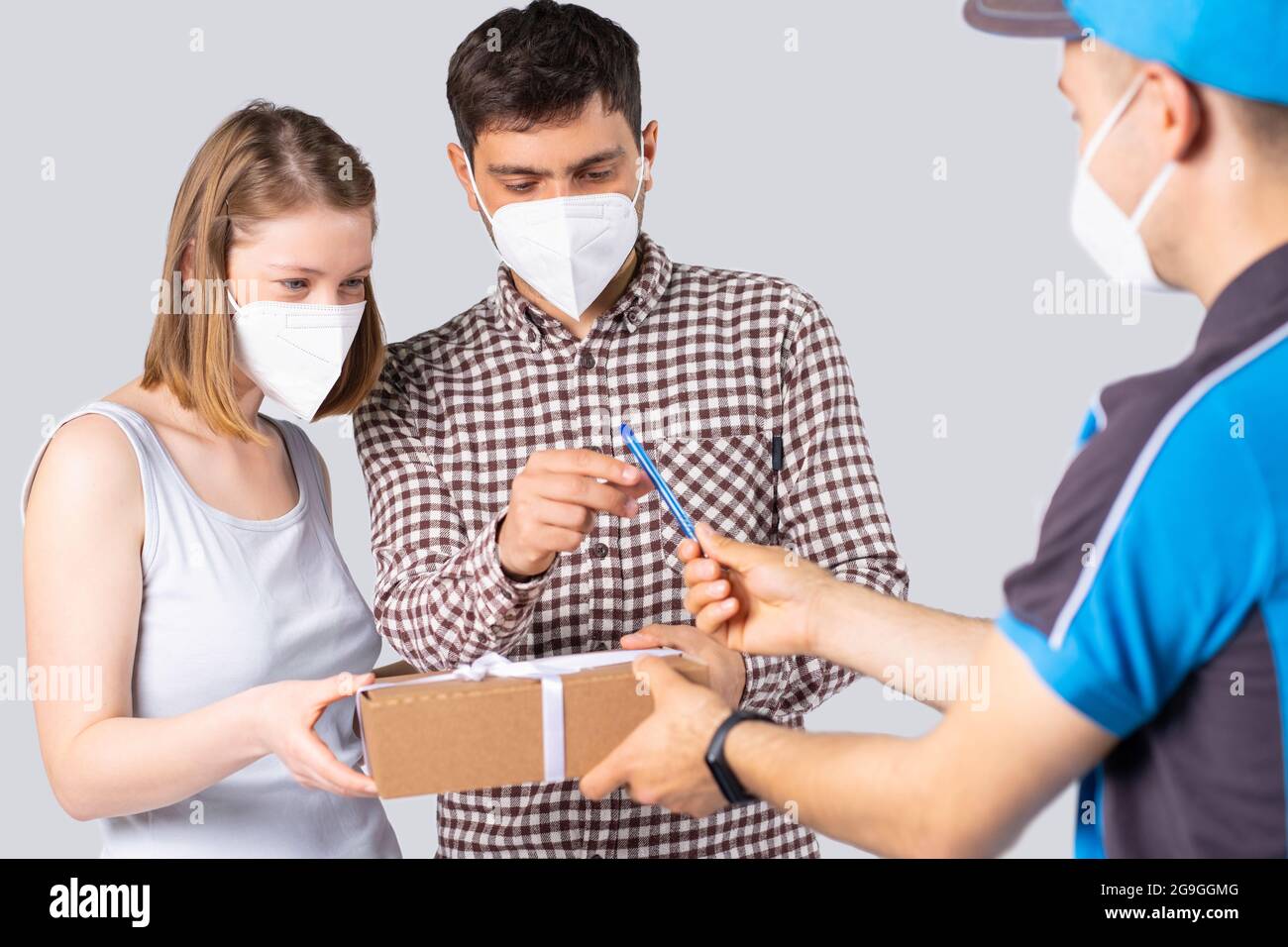 La giovane coppia in maschere mediche uomo e donna ha ricevuto il pacco dall'uomo di consegna e dà all'uomo penna per firmare per esso. Foto Stock