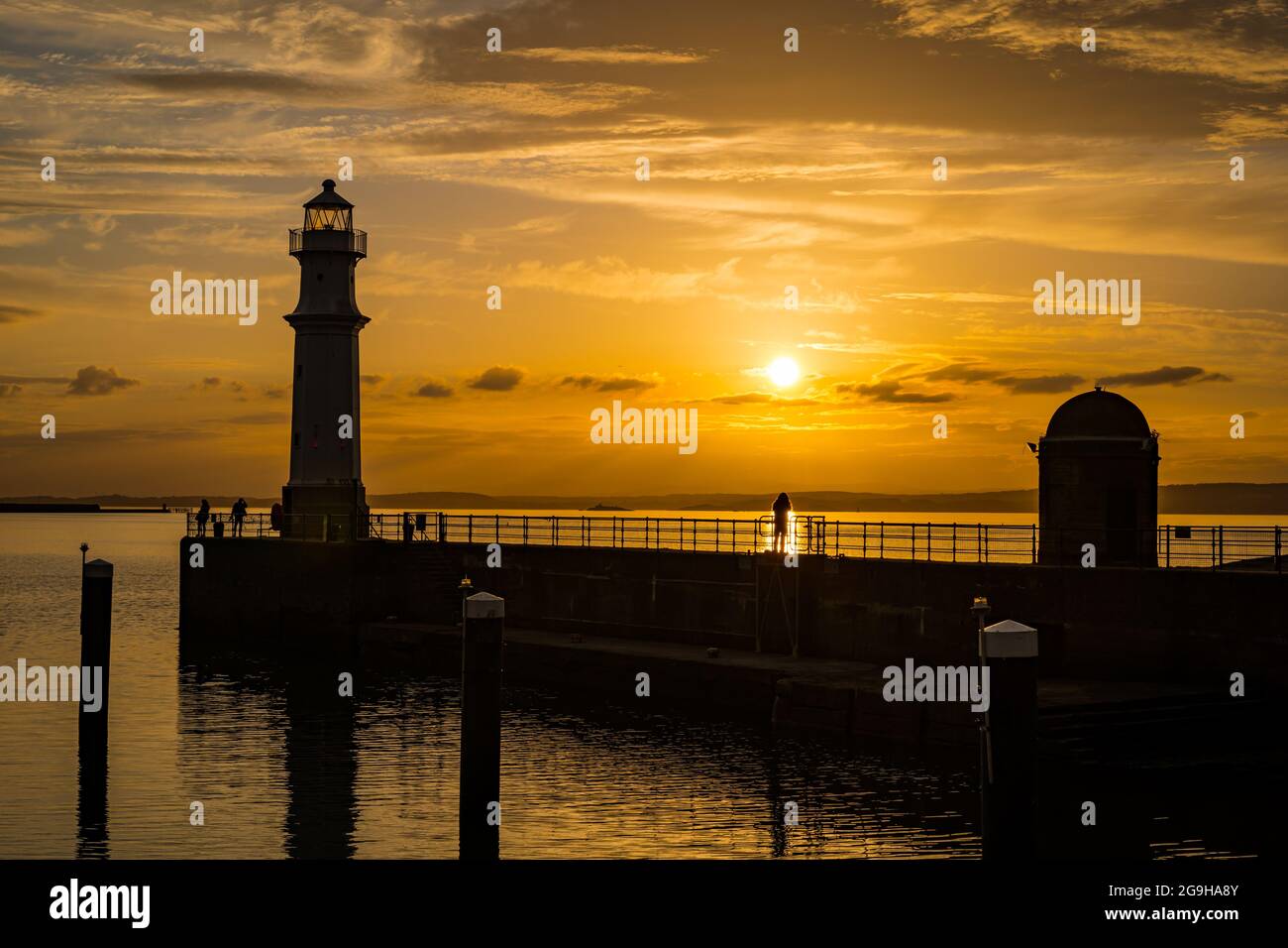 Le persone si sono sfrecciate sul molo del porto di Newhaven e sul faro in un colorato cielo arancione al tramonto, Edimburgo, Scozia, Regno Unito Foto Stock