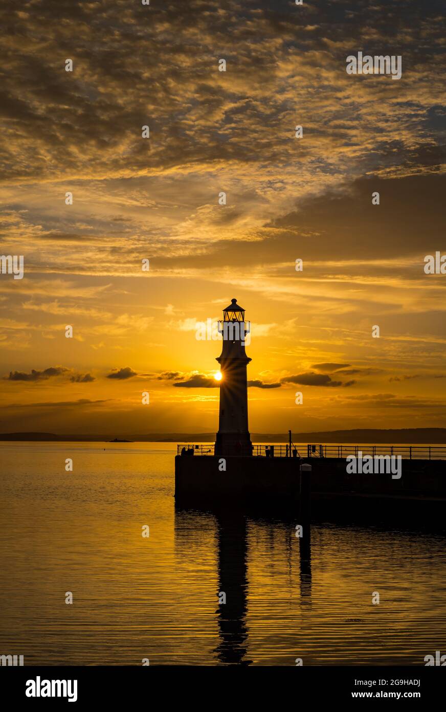 Il faro del porto di Newhaven si trova in un colorato cielo arancione con un'esplosione di sole al tramonto, Edimburgo, Scozia, Regno Unito Foto Stock