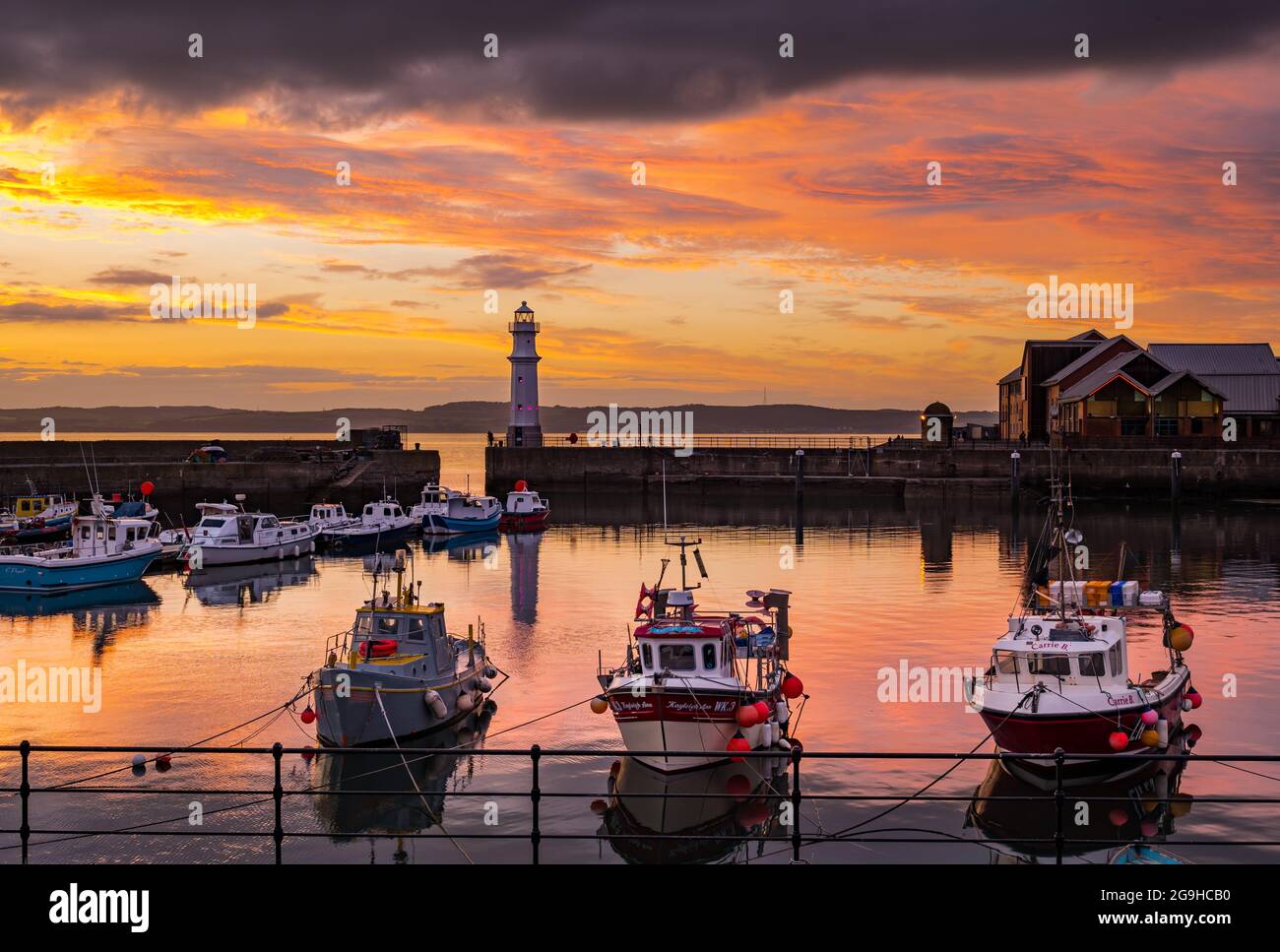Piccole barche da pesca colorate ormeggiate nel porto di Newhaven al tramonto con faro, Edimburgo, Scozia, Regno Unito Foto Stock