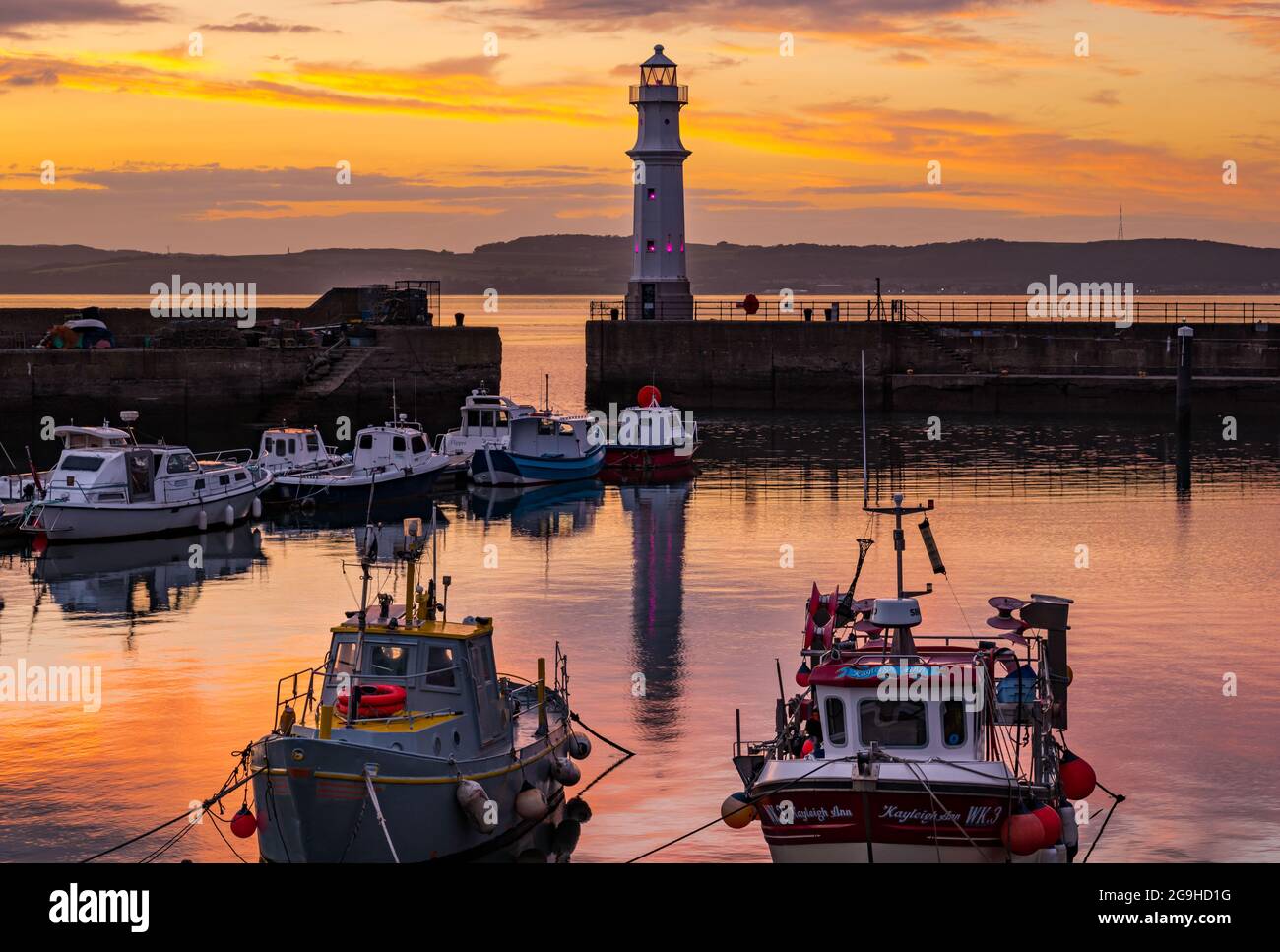 Piccole barche da pesca colorate ormeggiate nel porto di Newhaven al tramonto con faro, Edimburgo, Scozia, Regno Unito Foto Stock