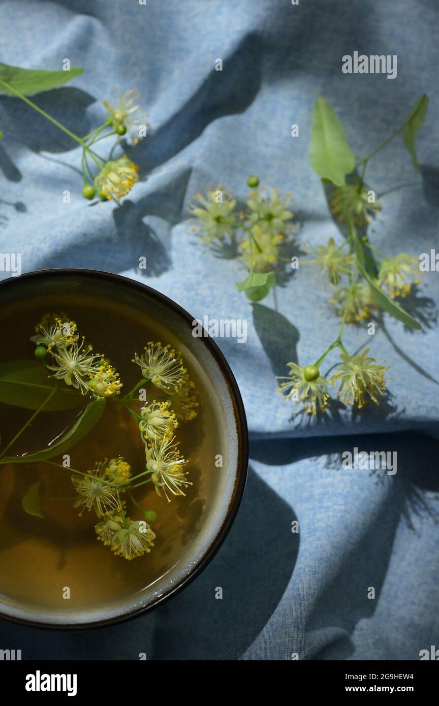 Tazza con tè tiglio, fiori e luce naturale Foto Stock