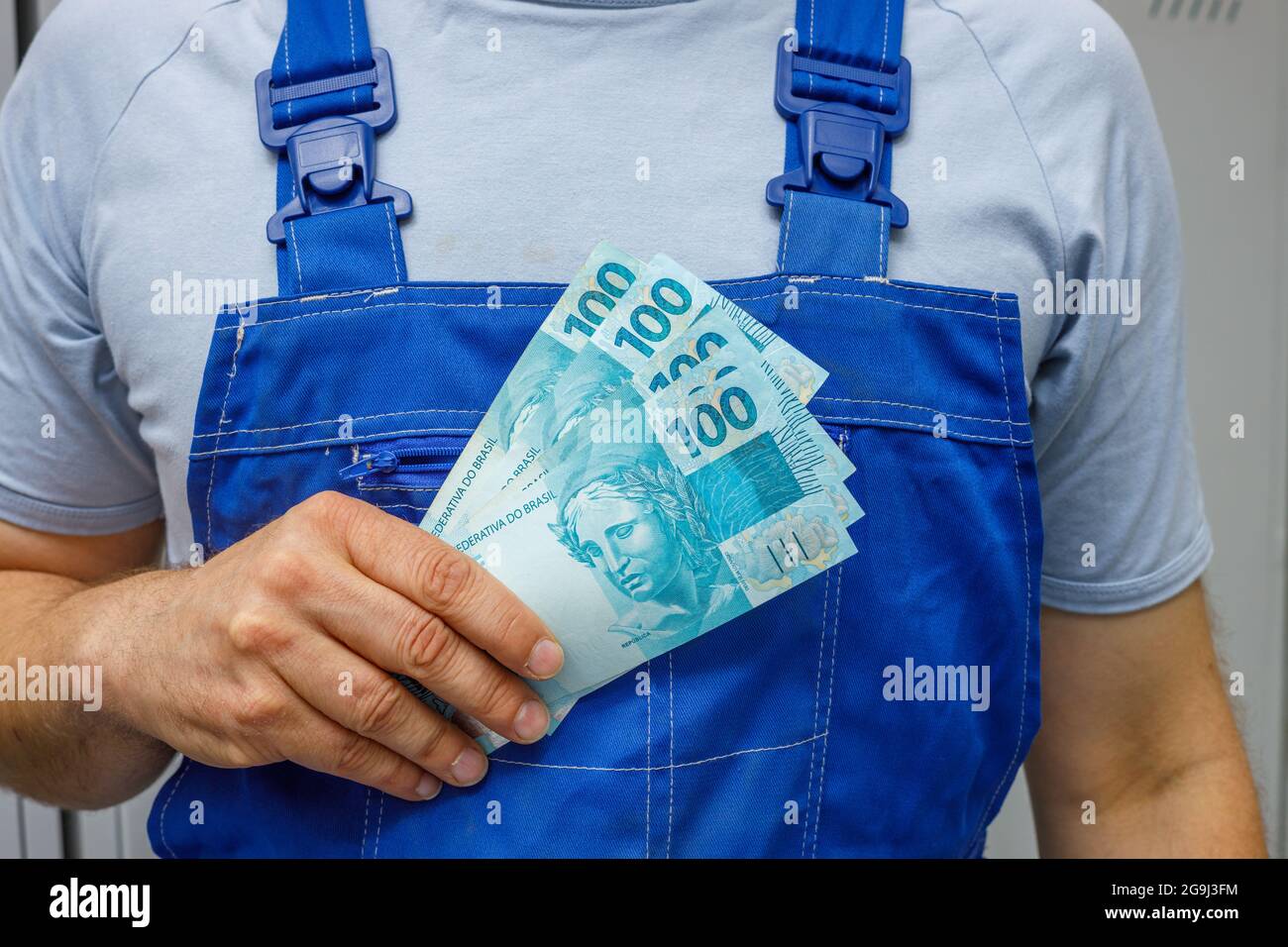 Un lavoratore brasiliano detiene denaro, cento banconote reali. Concetto di salario per professionisti e lavoratori Foto Stock