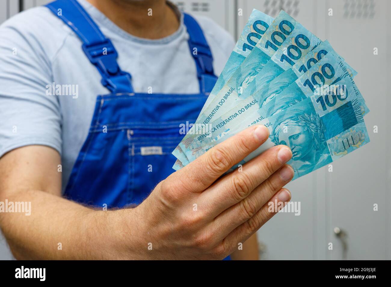 Lavoratore brasiliano mostrando denaro. Pacchetto di banconote di cento reais, stipendi di professionisti e lavoratori di colletti blu Foto Stock