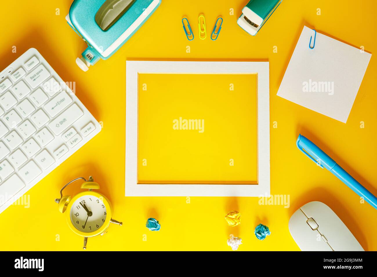 Un layout creativo di attrezzature per ufficio con una cornice al centro per una nota, colori giallo, bianco e blu Foto Stock