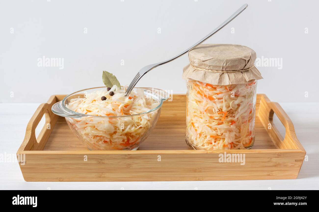 Sauerkraut in un vaso e in una ciotola. Crauti con carote in un vassoio di legno su fondo bianco. Cibo fermentato. Insalata di cavolo. Foto Stock