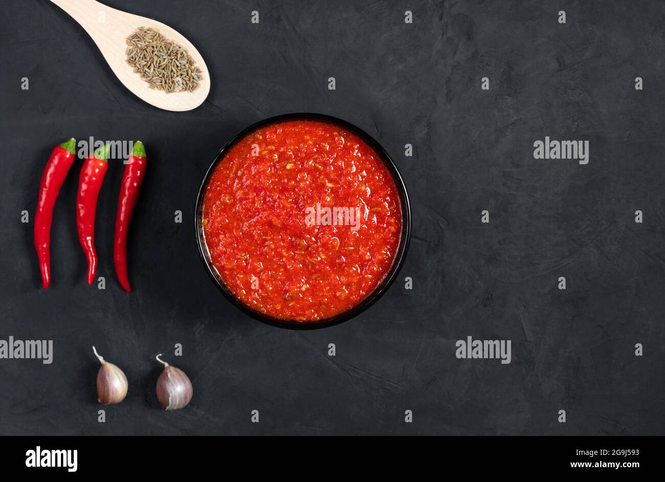 Salsa di Harissa su fondo nero. Adjika salsa piccante di peperoni. Vista dall'alto. Spazio per il testo. Foto Stock