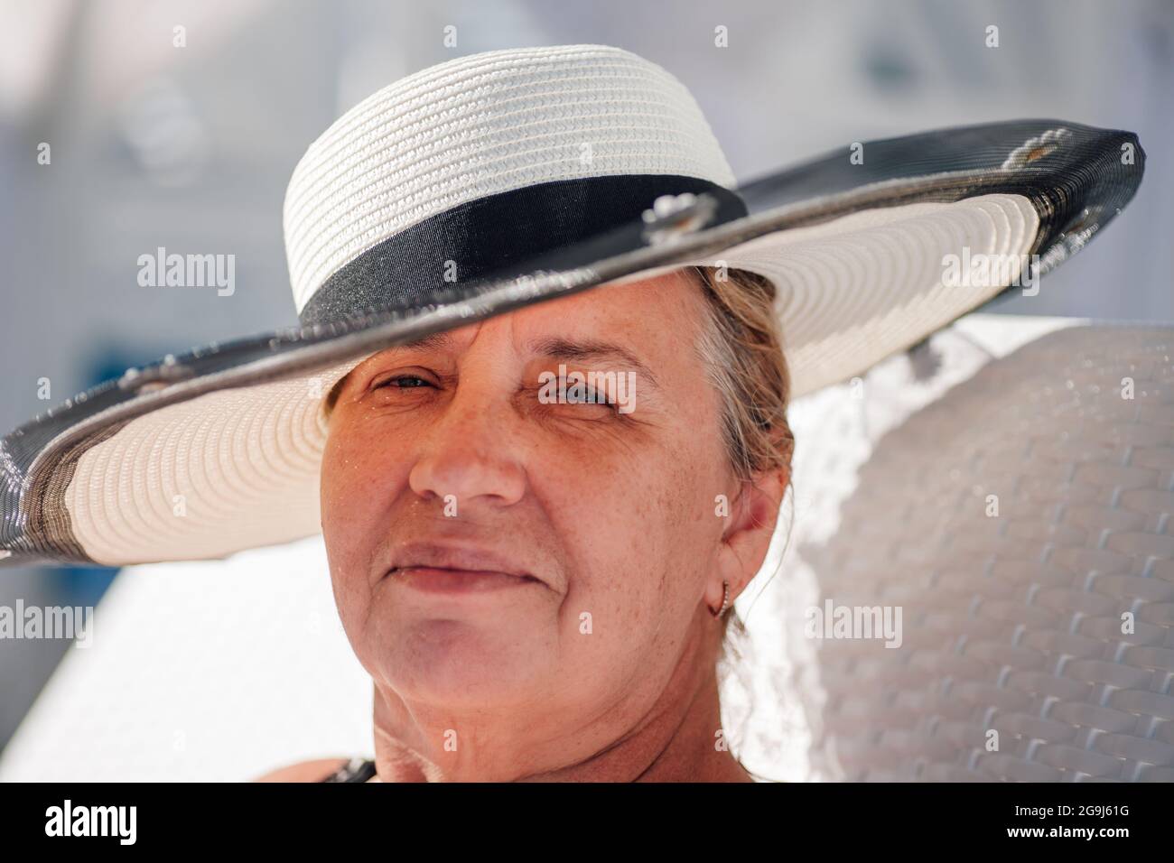 Una donna in un cappello di paglia. Ritratto in primo piano di una donna adulta sorridente in un cappello di paglia bianca in una giornata di sole brillante Foto Stock