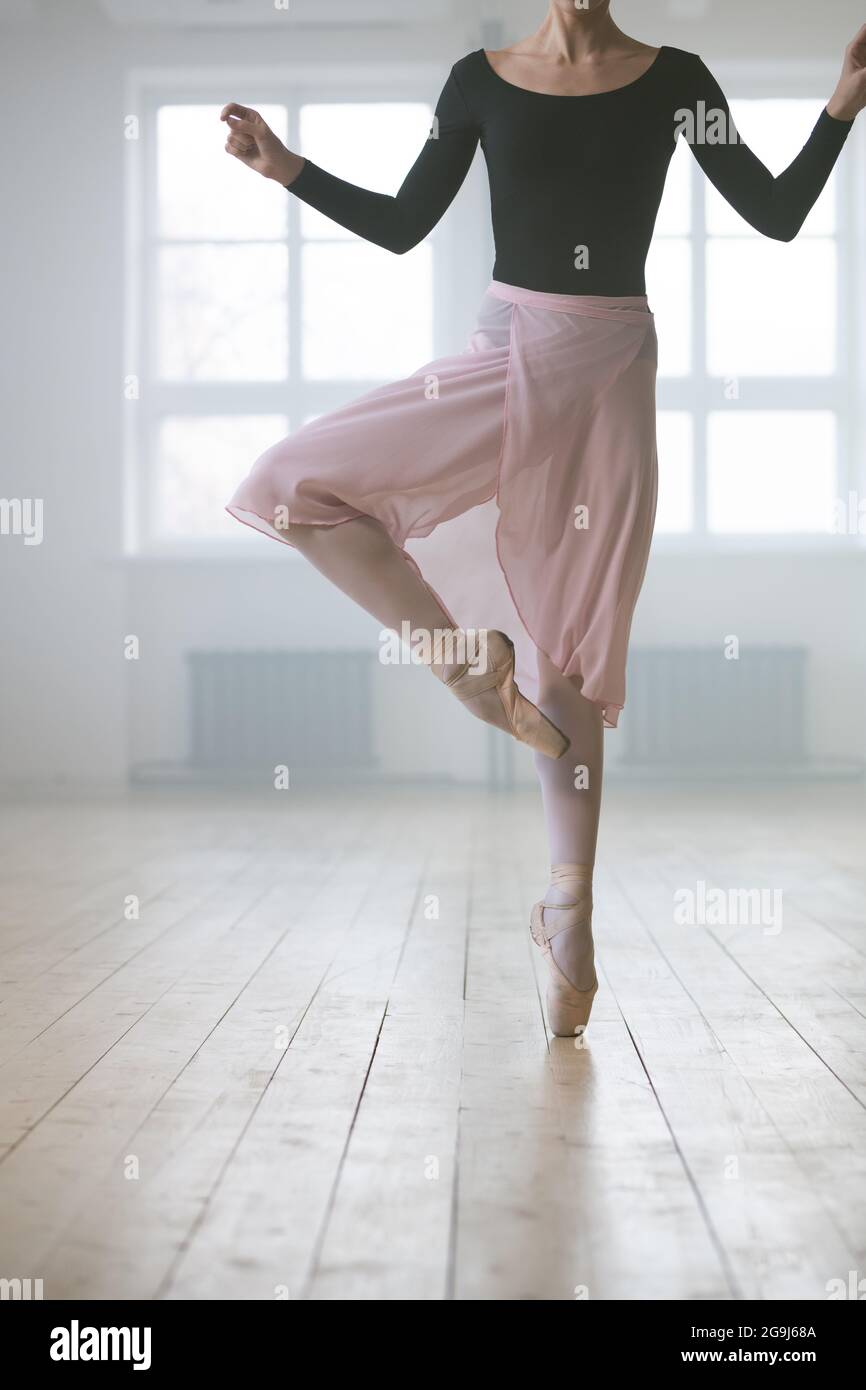 Primo piano di donna in abito tutu e in scarpe pointe stare in piedi su una gamba e praticare il balletto in studio Foto Stock
