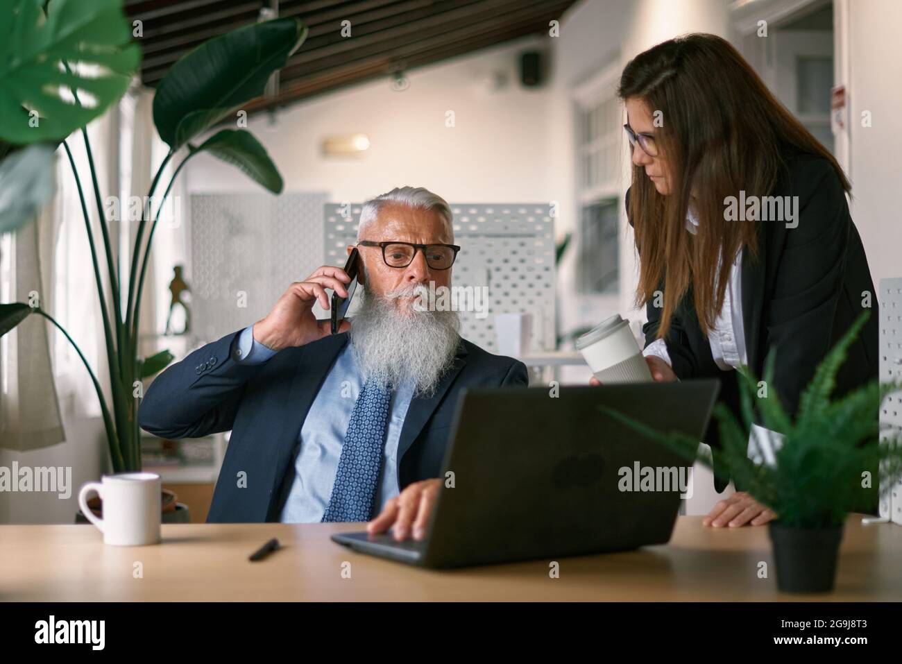 Uomo d'affari senior che parla su smartphone vicino a un collega Foto Stock