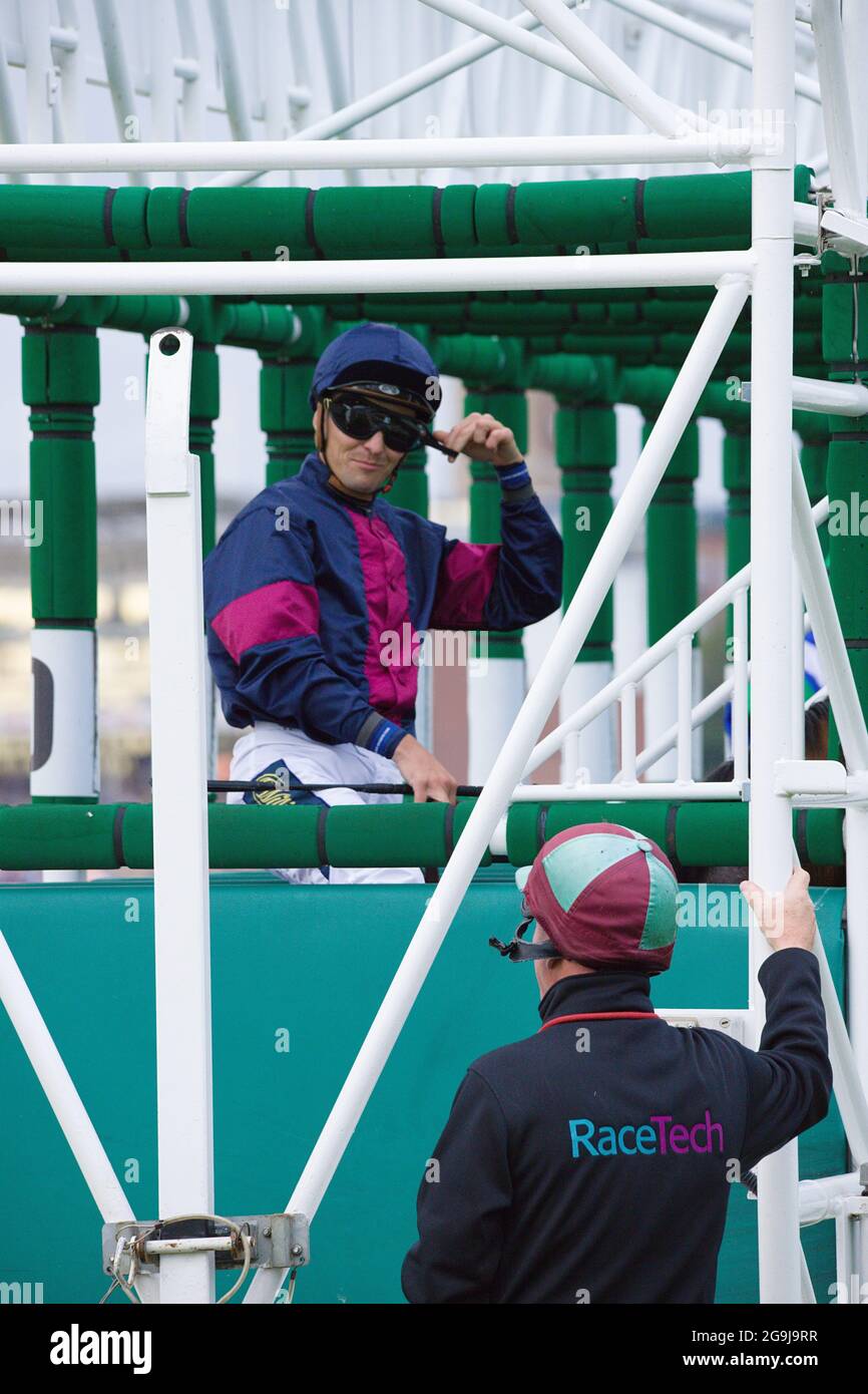 Jockey Kevin Stott che chiacchiera con il personale dell'ippodromo mentre si trova nelle porte di partenza dell'ippodromo di York. Foto Stock