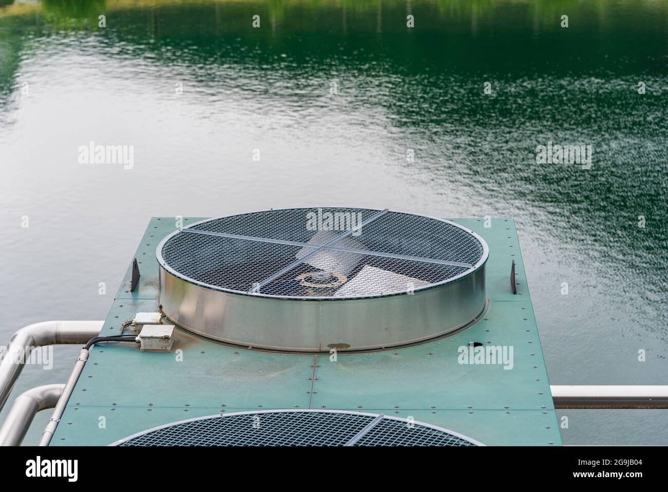 Sistema di raffreddamento industriale. Radiatore e ventilatori situati sulla riva del lago. Pale del rotore visibili, rete di sicurezza, tubazioni. Foto Stock