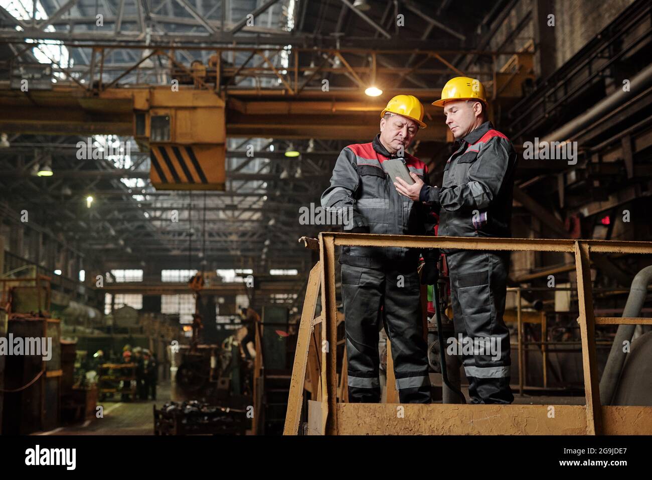 Due lavoratori manuali in abbigliamento da lavoro che utilizzano tablet digitali e discutono lavorare mentre si è in piedi nella pianta Foto Stock