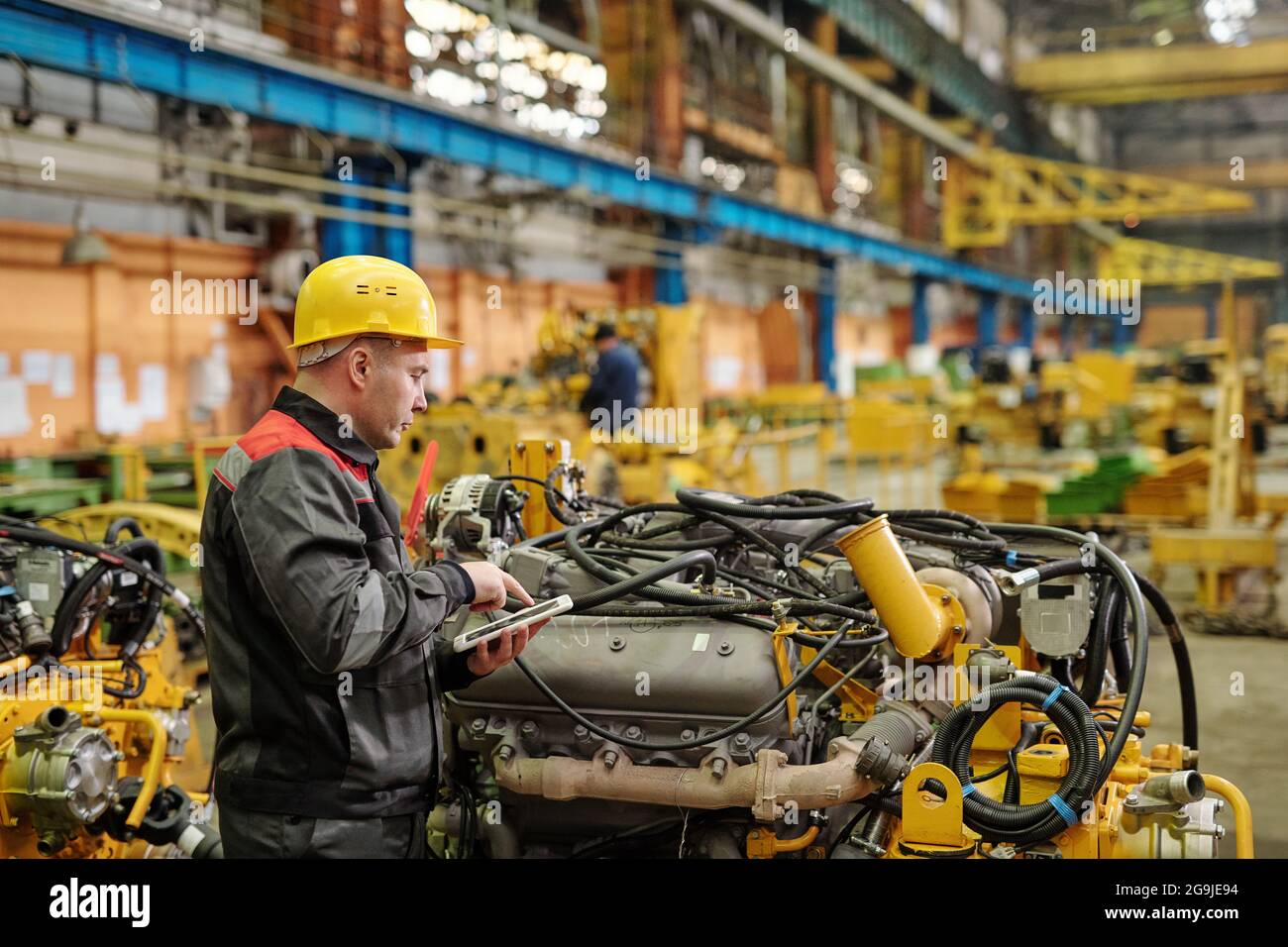 Ritratto di un ingegnere maturo in abbigliamento da lavoro che guarda al funzionamento della fotocamera in fabbrica di macchine Foto Stock