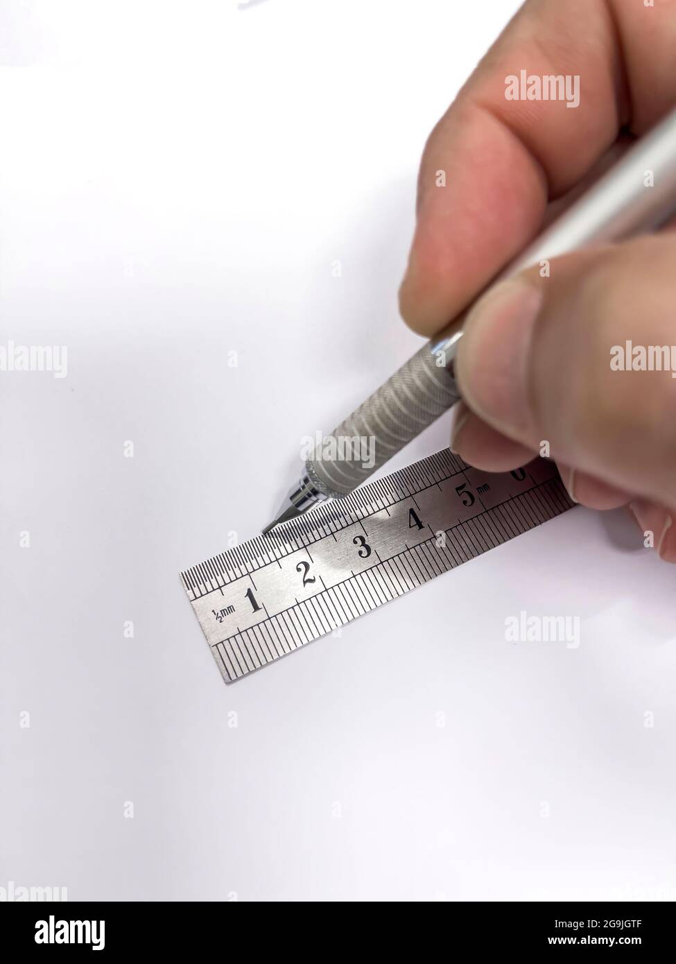 mano con una matita meccanica in metallo che fa una linea retta con un righello millimetrico metallico su un foglio di carta vuoto, fuoco selettivo nel righello, v Foto Stock