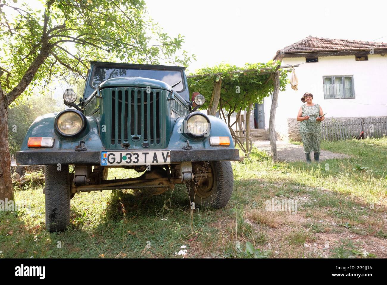 PADES, ROMANIA - LUGLIO 27: Un vecchio M461 ARO - la jeep rumena - in un fondo rurale di Cerna Sat, sullo sfondo una donna contadina di fronte alla sua casa colonica Foto Stock