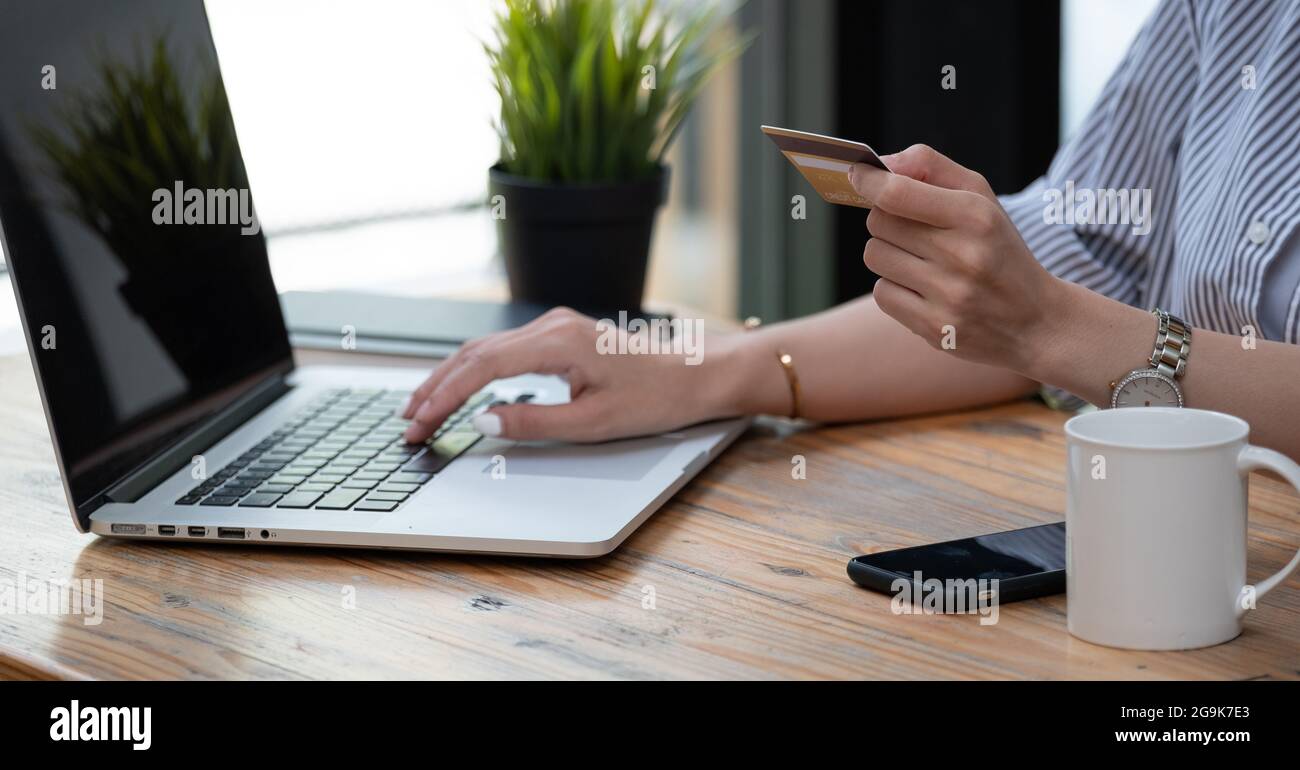 Close up mano di donna asiatica che acquista online con computer portatile e carta di credito a casa Foto Stock